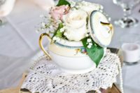 a stack of books, notes, a doily, a teapot, a strand of pearls and pink and white roses and baby’s breath
