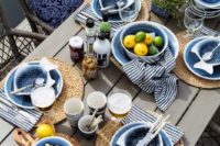 a stylish and simple nautical bridal shower setting with an uncovered table, wicker chargers, blue and fish plates plus a citrus centerpiece