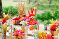 a super bright tropical bridal shower with a gold tablecloth, colorful floral arrangements, colored glasses and gold touches