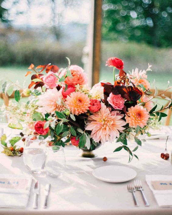 a super colorful wedding centerpiece of orange and pink dahlias, burgundy and pink ranunculus, greenery and some berries