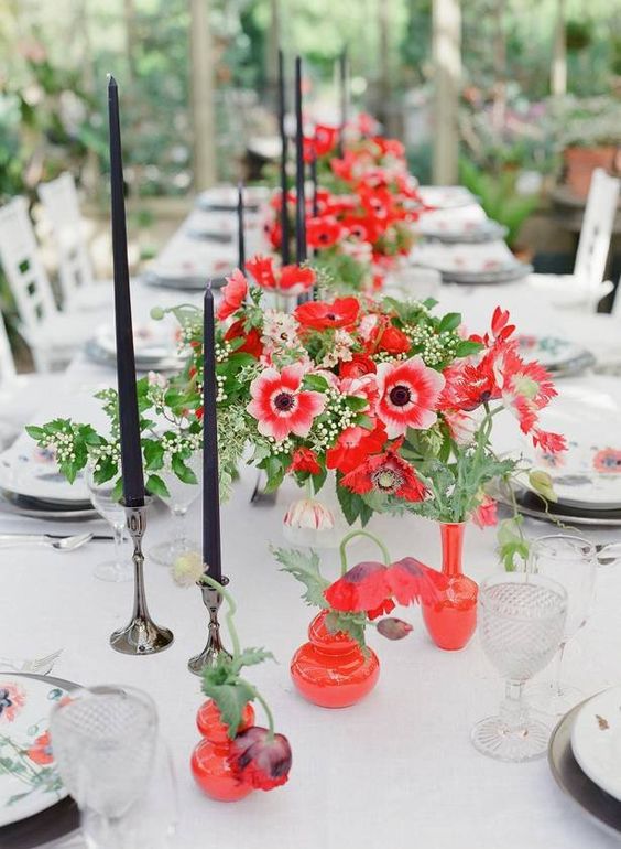 a super colorful wedding centerpiece of red anemones and greenery paired with black candles and red vases is wow