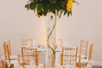 a tall wedding centerpiece of much textural greenery and some sunflowers and twigs over them