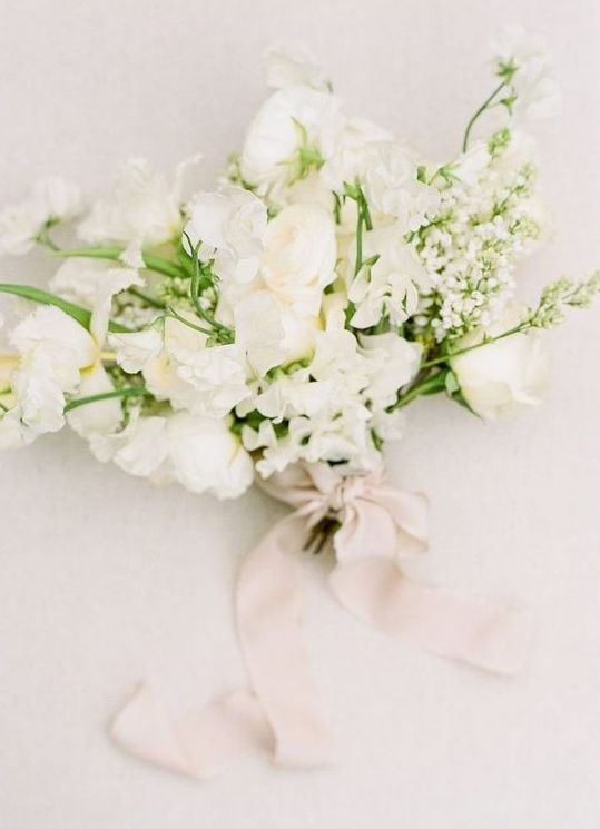 a textural and dimensional white wedding bouquet with some greenery and blush ribbons