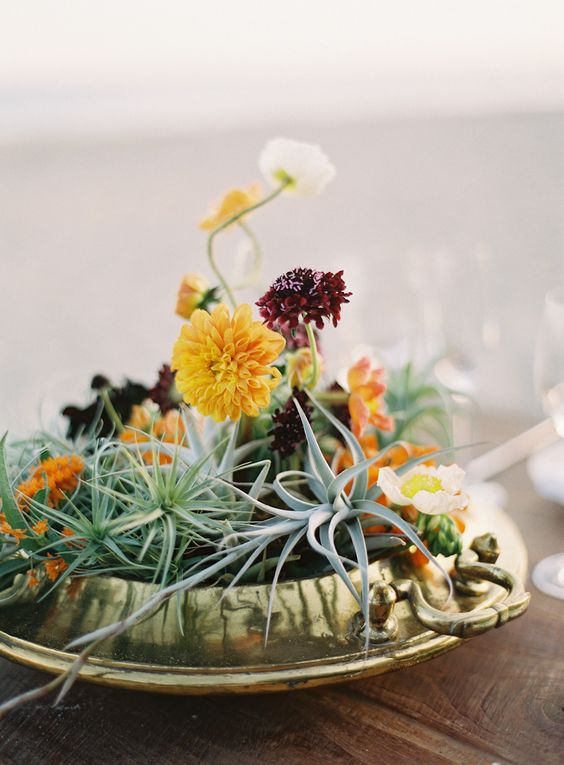 a textural wedding centerpiece of a gilded bowl, air plants, bold yellow and burgundy blooms is a great idea for a fall wedding