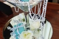 a themed centerpiece of a mirror, a large glass, pearls, roses, rhinestones and tiffany blue gifts