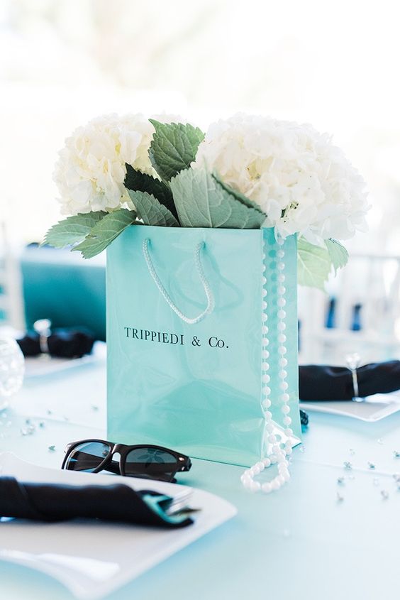 a tiffany blue paper bag centerpiece with white hydrangeas and greenery, pearls and sunglasses
