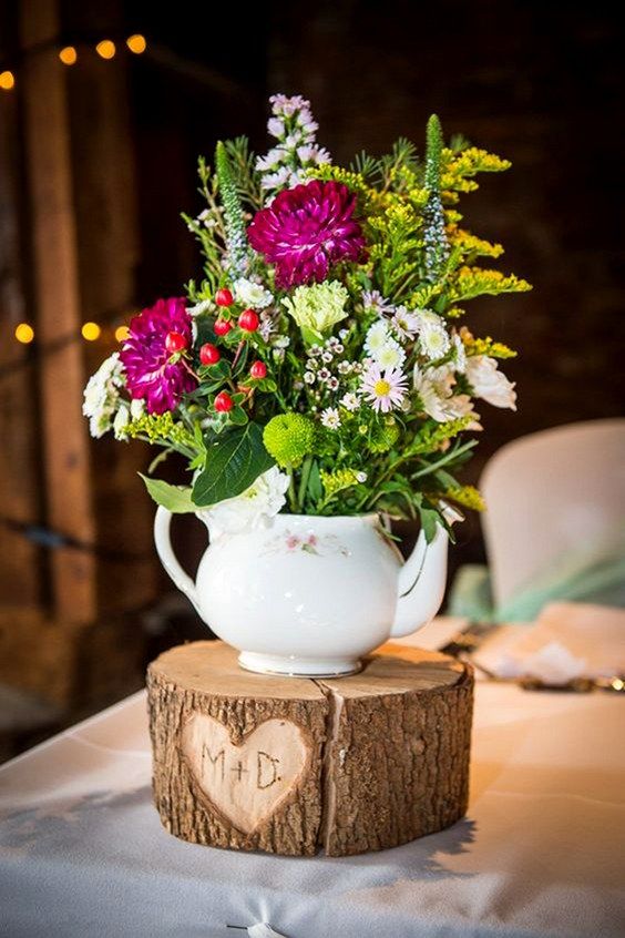 a tree stump with a cutout heart and monograms, a white teapot with greenery and bright flowers