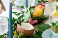 a tropical bridal shower table setting with greenery, coconuts, blooms and blue candles and porcelain