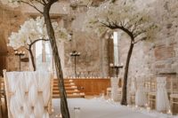 a unique wedding ceremony space with curved trees with cherry blossom, chairs with white textiles and lots of candles looks unbelievable