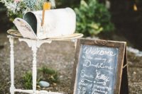 a vintage whitewashed mailbox placed on a side table, pastel blooms next to it and a chalkboard sign