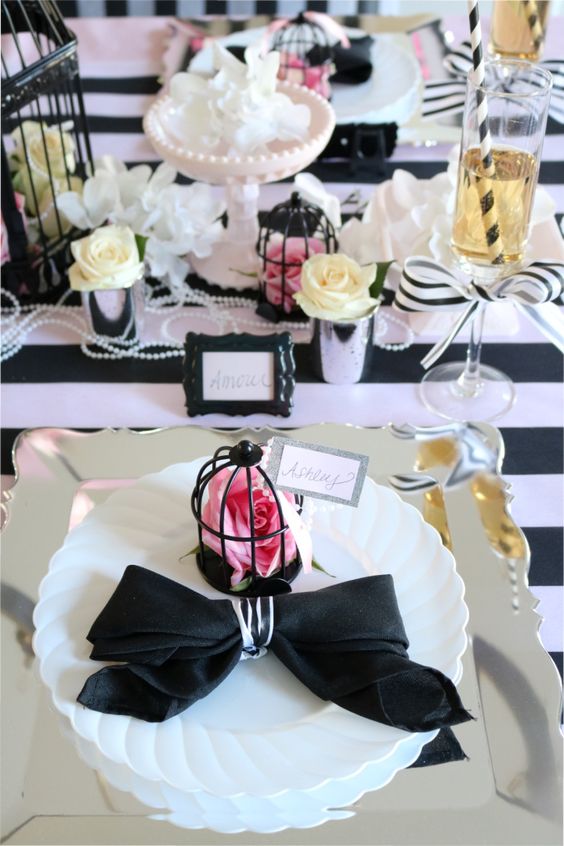 a whimsical Parisian themed tablescape with a striped tablecloth, a black cage, neutral and pink blooms and some pearls is chic