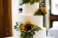 a white textural wedding cake decorated with greenery and sunflowers for a bold and cool look