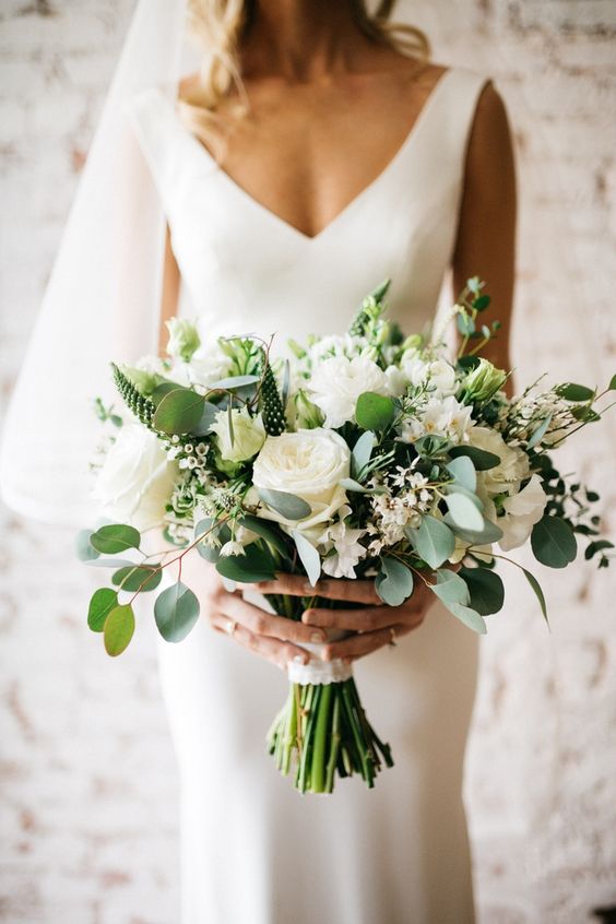 a white wedding bouquet with peonies and roses, greenery and much texture and with a white lace wrap