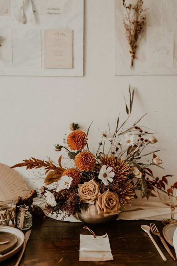 an earthy-tone wedding centerpiece of orange dahlias, coffee-colored roses, white blooms and dried flowers plus grasses