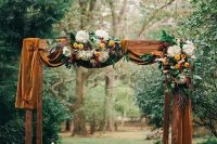 an elegant and refined rustic fall wedding arch with mustard velvet, white hydrangeas, yellow dahlias, burgundy blooms and greenery is a very stylish and cool idea