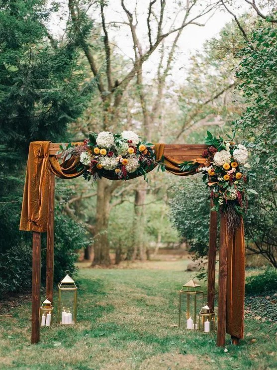 an elegant and refined rustic fall wedding arch with mustard velvet, white hydrangeas, yellow dahlias, burgundy blooms and greenery is a very stylish and cool idea