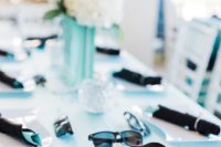 an elegant bridal shower tablescape with a tiffany blue tablecloth, black napkins with rings, white blooms and sunglasses