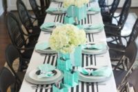 an elegant table setting with a striped black and white table runner, white and black plates, tiffany blue napkins and paper bags plus white bloom centerpieces