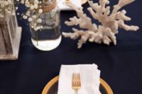 an elegant tablescape done with a navy tablecloth, corals, a gilded charger and cutlery, a baby’s breath for a centerpiece