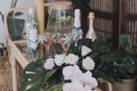 an elegant tropical beverage cart with white blooms, tropical leaves, paper wrapped bottles and leaf arrangements
