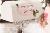 an elegant white vintage mailbox with a pink sticker with the couple’s names and some pink blooms and greenery