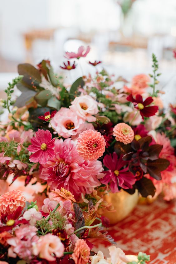 an extra bold wedding centerpiece of pink dahlias, orange dahlias, burgundy and purple blooms, dark foliage and greenery