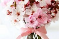 cherry blooms in a glass vase with a pink bow on it makes up a cool and lovely wedding centerpiece for spring