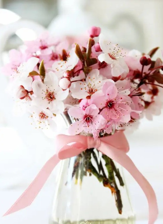 cherry blooms in a glass vase with a pink bow on it makes up a cool and lovely wedding centerpiece for spring