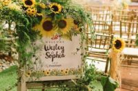 cool rustic wedding decor of greenery and sunflowers put on a wedding sign with painted sunflowers