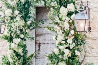 a wedding arch made of greenery and white blooms coming out of pots and climbing up the wall is a creative idea
