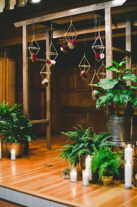 a wedding ceremony space done with potted greenery, candles and flowers suspended in himmeli decorations