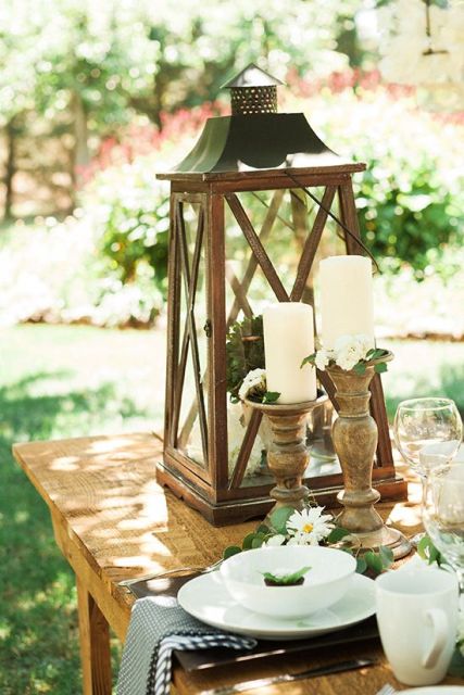candles in wooden candleholders and a large candle lantern with greenery for styling the table