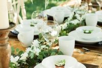 a cozy rustic setting with a greenery and white bloom runner, candles in wooden candleholders, printed napkins