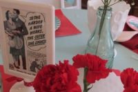 a bright tablescape with a blue tablecloth, a red table runner, bold red carnations, baby’s breath and some vintage card decor