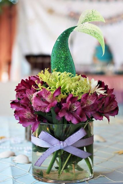 a fun mermaid bridal shower centerpiece of purple and green blooms and a sparkling mermaid tail is cool