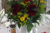 a bold vintage wedding centerpiece composed of a white jug with greenery, burgundy and yellow blooms, and vintage jars with candies around