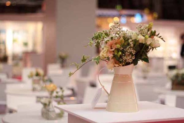 a rustic wedding centerpiece of an ivory metal jug with blush and white blooms and greenery is a chic idea for a spring or summer wedding