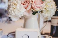 a delicate rustic wedding centerpiece of a creamy metal jug with white and blush blooms and a table number is easy to make yourself