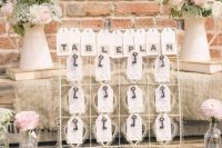 a whimsical wedding seating plan surrounded with neutral metal jugs with pastel blooms and greenery as centerpieces or just arrangements