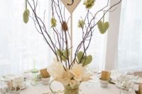a creative spring wedding centerpiece of a green jug, branches with green fabric hearts, white blooms and a heart-shaped table number is cool