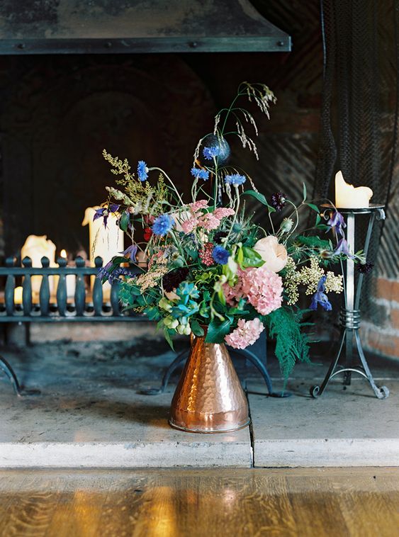 a beautiful and dimensional wedding centerpiece of a copper jug, bright blooms and lots of greeneyr for a summer wedding