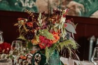 a beautiful boho fall wedding centerpiece of a green ribbed jug, bold blooms and greenery plus privet berries