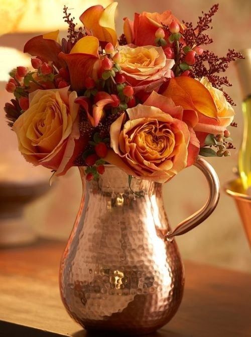 a beautiful hammered copper jug with orange roses, berries and a bit of greenery is a bright solution for a fall wedding
