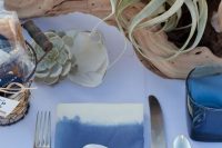 a beautiful sea-inspired bridal shower tablescape with a white tablecloth and an ombre napkin, driftwood and air plants and succulents