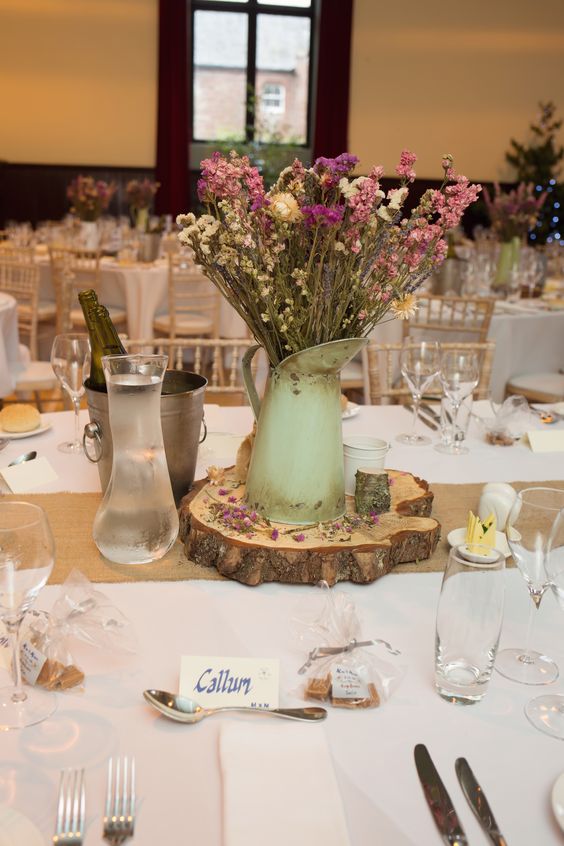 a boho summer wedding centerpiece of a wood slice, a green metal jug with boho dried and fresh blooms is amazing