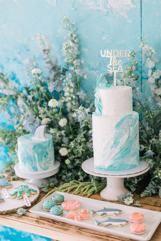 a bold mermaid bridal shower dessert table with white and turquoise wave cakes, turquoise macarons and shark and starfish cookies