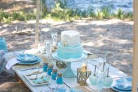 a bold mermaid bridal shower table with blue plates, an ombre white to turquoise cake, sea-inspired cookies and lanterns