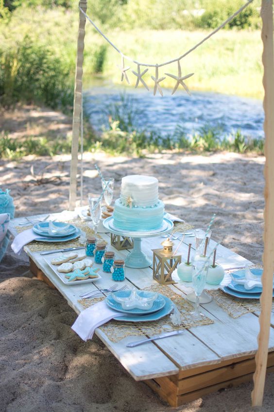 a bold mermaid bridal shower table with blue plates, an ombre white to turquoise cake, sea-inspired cookies and lanterns