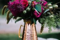 a bold wedding centerpiece of a copper jug and bold burgundy and fuchsia blooms and greenery and bunny tails for a fall wedding