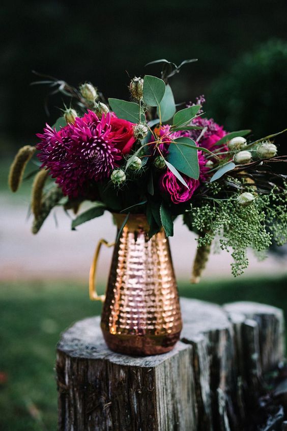 a bold wedding centerpiece of a copper jug and bold burgundy and fuchsia blooms and greenery and bunny tails for a fall wedding